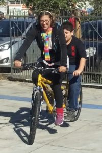 Na foto Profª Isabel andando de bicicleta Tadem com o usuário Pedro Henrique, eles estão na frente da ACIC